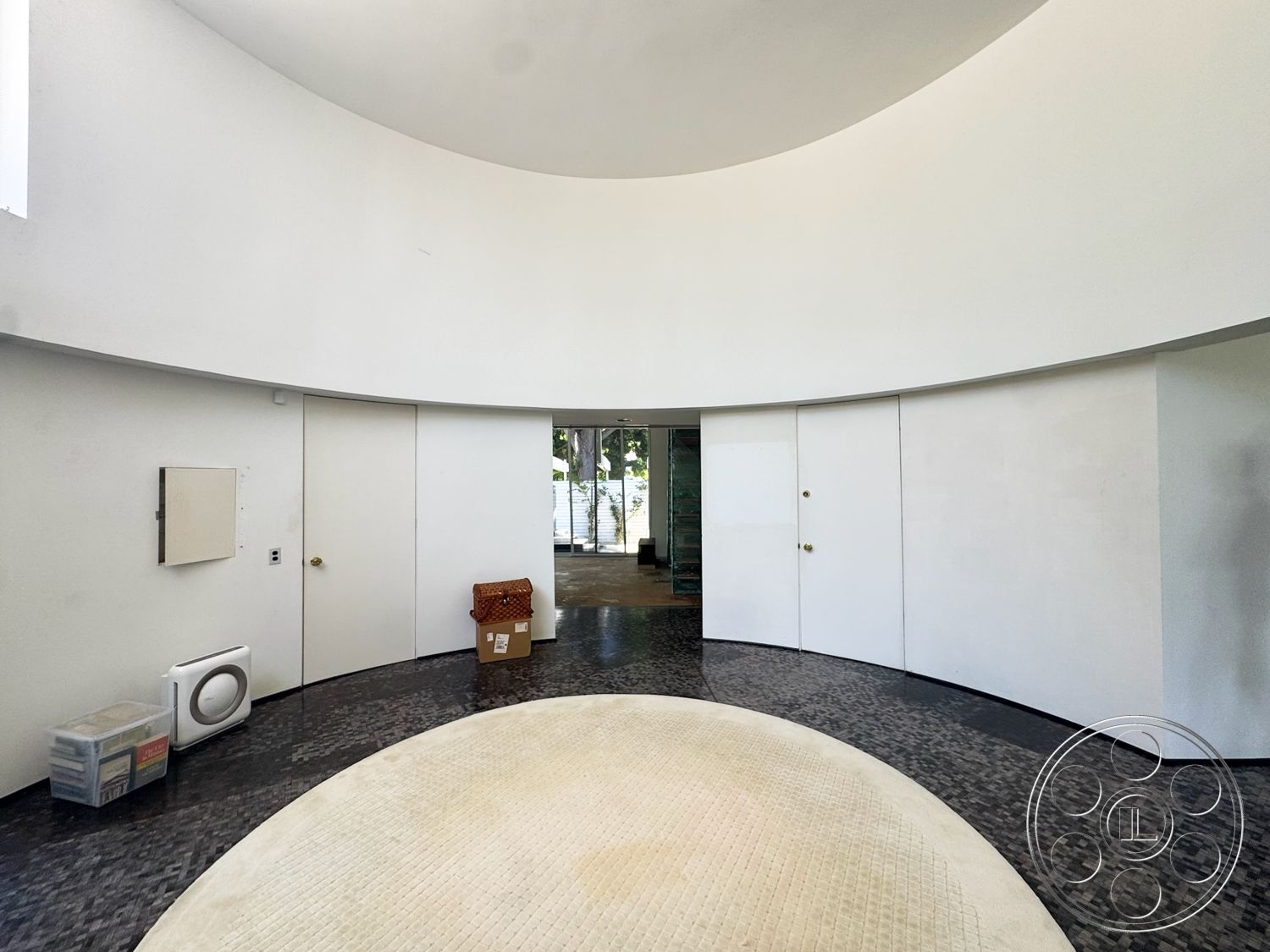 MCM 28 - minimalist design elements, round area rug, black tile flooring, natural light through large windows, curved white walls, double doors with brass knobs, built-in wall units, flowing circular layout