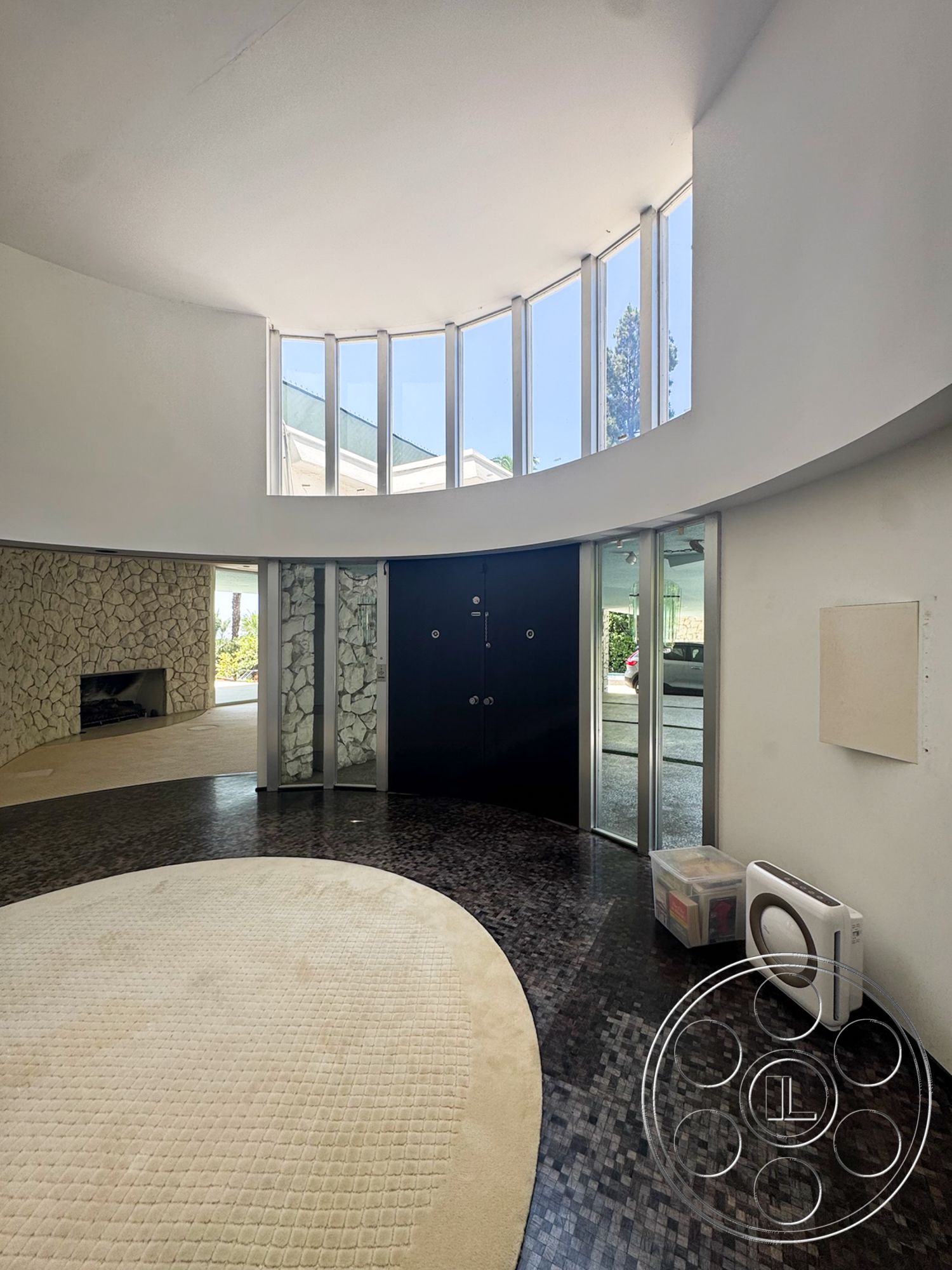 MCM 28 - minimalist decor, bright natural light, open concept layout, floor-to-ceiling windows, vaulted ceiling, dark hardwood flooring, modern architectural style, curved wall design, stone feature wall, black double doors, beige circular area rug
