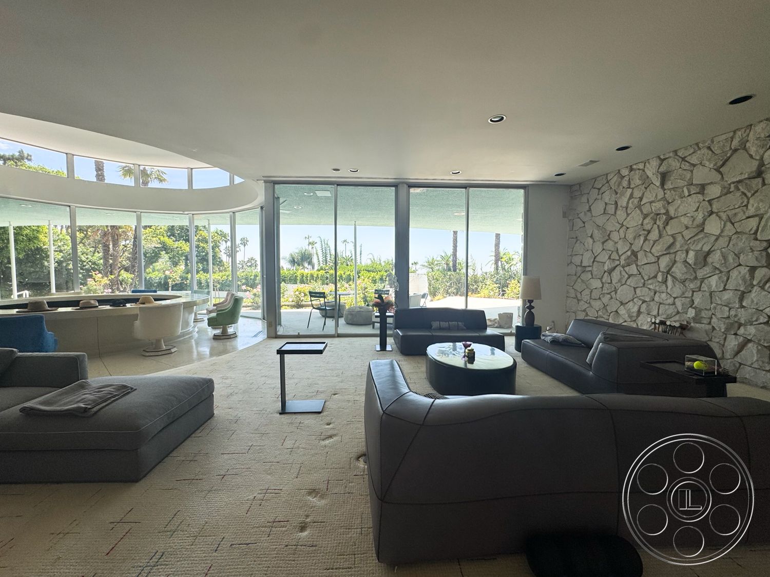 MCM 28 - natural light, open floor plan, modern coffee table, glass windows, vaulted ceiling, mid-century modern style, stone feature wall, outdoor garden view, textured carpet flooring, modern leather sectional sofa, curved glass walls