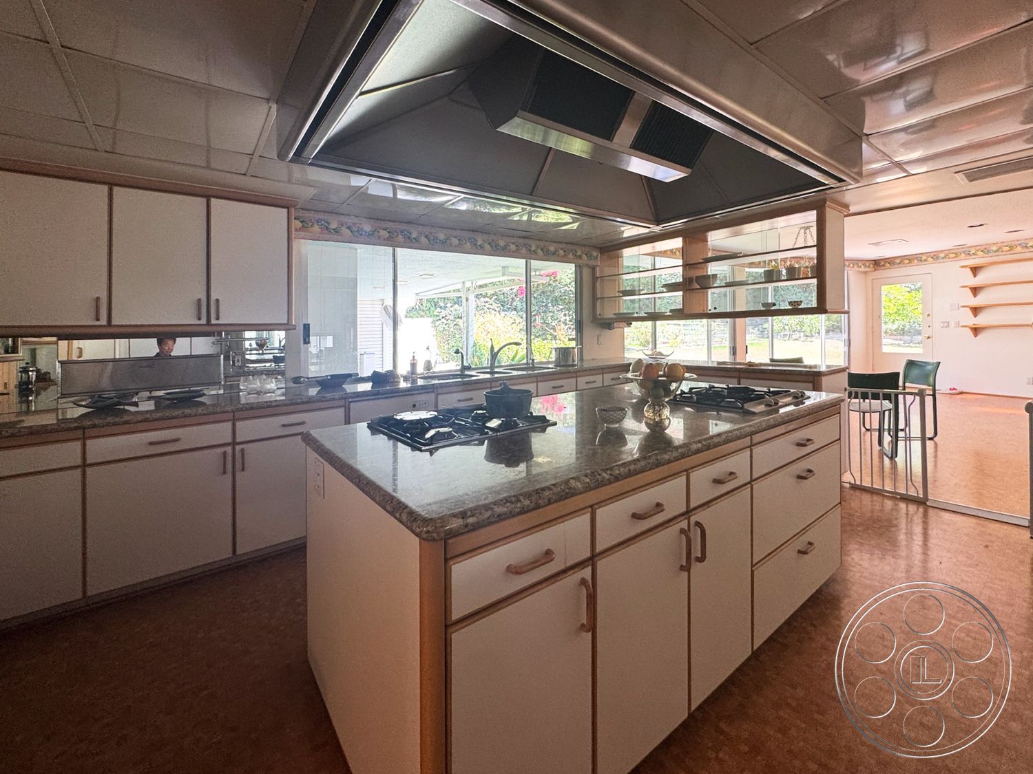 MCM 28 - open floor plan, textured ceiling, vinyl flooring, interior kitchen space, granite kitchen countertops, large windows with garden view, white laminate kitchen cabinets, exterior access door, stainless steel exhaust hood, breakfast bar seating area, kitchen island with gas cooktop, built-in glass shelves