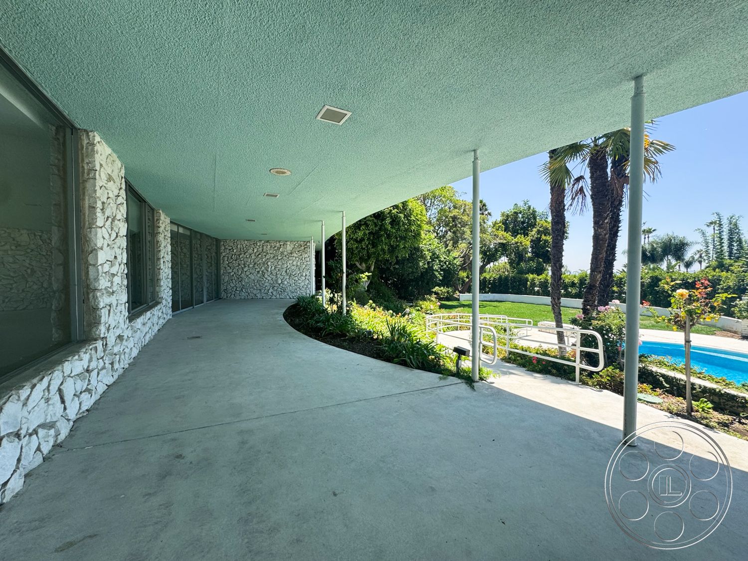 MCM 28 - exterior, large glass windows, pool area, concrete walkway, garden area, exposed stone wall, flat roof design, palm trees landscaping, smooth ceiling finish, curved porch, lawn with flowering plants