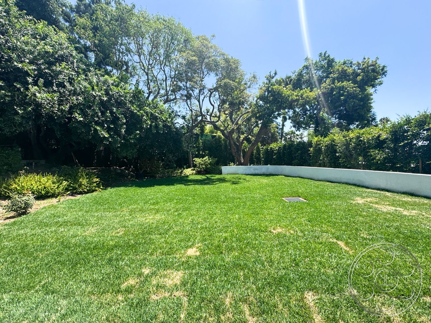 MCM 28 - exterior, green grass, surrounding trees, manicured lawn, backyard oasis, sunny setting, landscape greenery, curved concrete retaining wall
