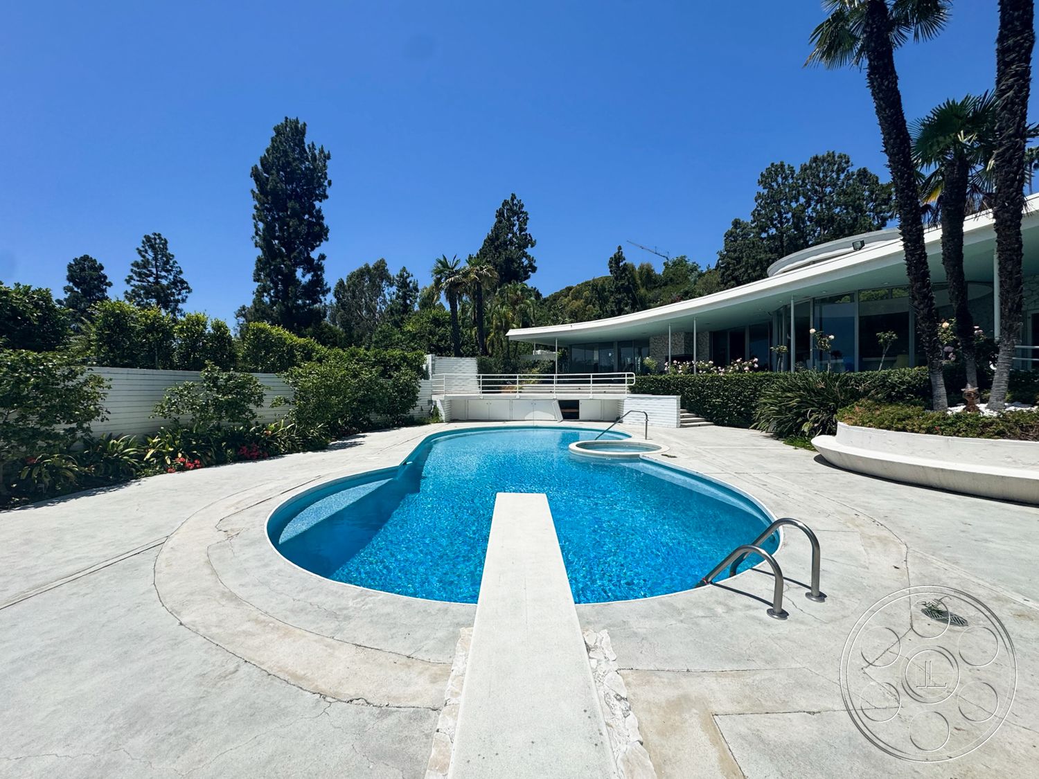 MCM 28 - exterior, landscaped garden, flat roof, clear blue sky, tropical palm trees, concrete pool deck, glass wall, oval swimming pool, modern house design, low-profile landscaping, stone wall seating, poolside handrail