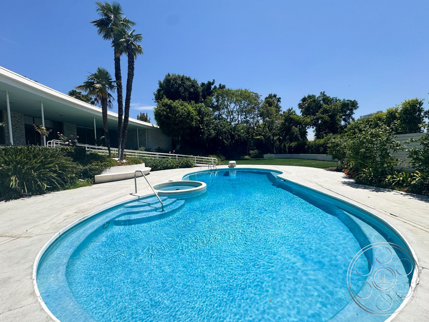 MCM 28 - exterior, landscaped garden, lush greenery, palm trees, single-story home, white exterior walls, concrete pool deck, blue pool water, sunny outdoor setting, sloped lawn, oval swimming pool, aluminum railings