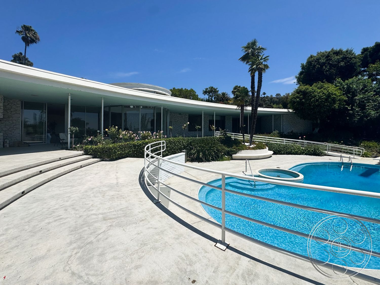 MCM 28 - exterior, lush greenery, glass sliding doors, rectangular swimming pool, mid-century modern style, vaulted roof, outdoor pool area, landscaped garden area, concrete patio floor, white metal railing, curved concrete steps, flat roof architecture, palm tree surroundings