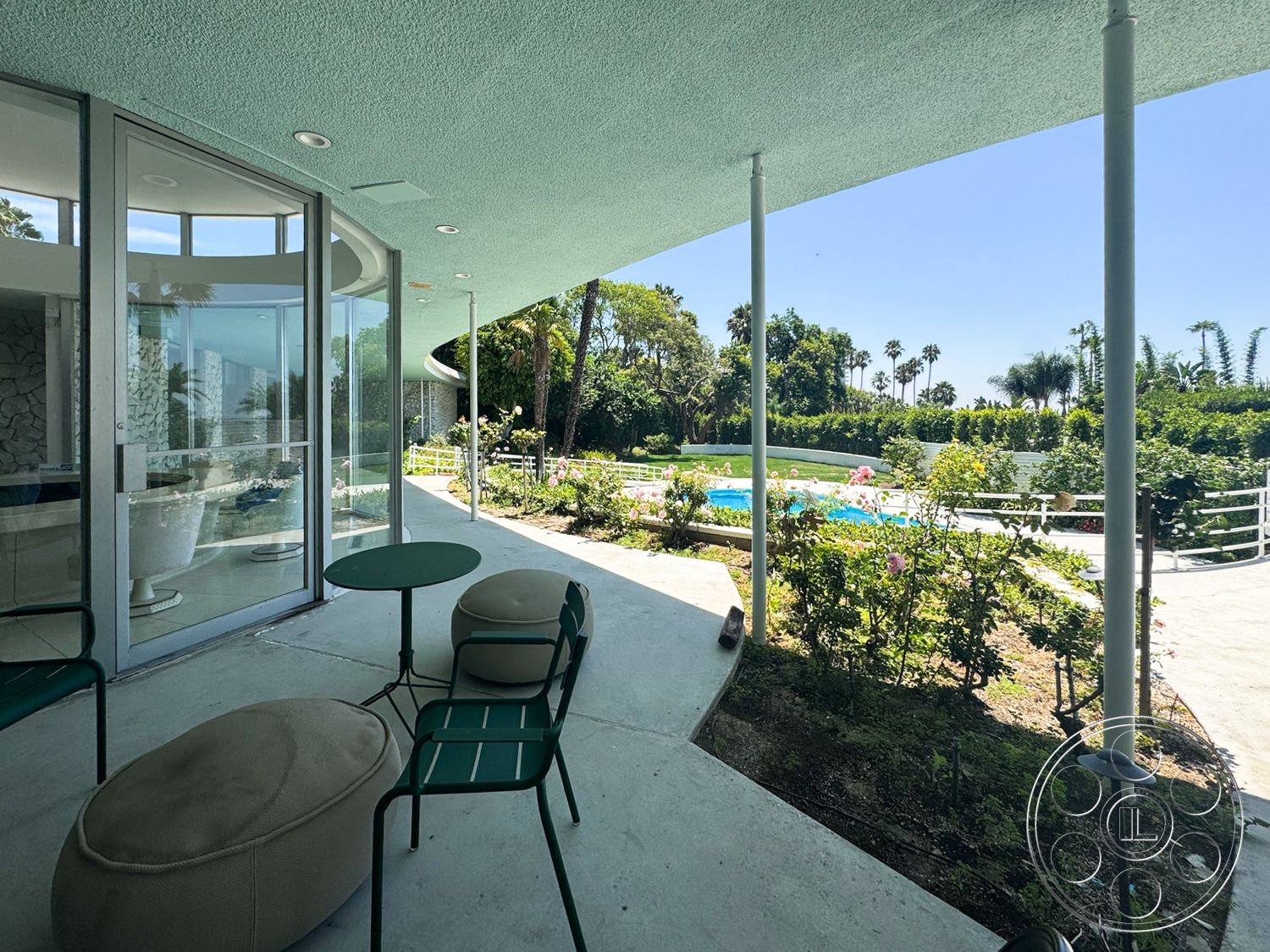 MCM 28 - exterior, rectangular pool, stone feature wall, green painted ceiling, metal patio furniture, concrete patio flooring, glass door system, tropical palm tree view, curved overhang roof, modern landscaping with rose bushes, lawn area with grassy landscape