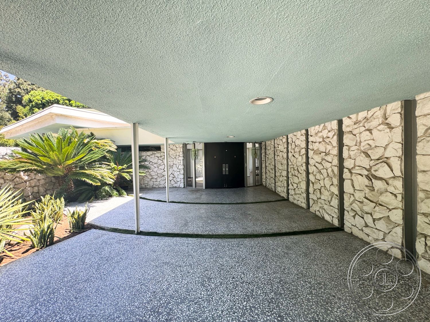 MCM 28 - exterior, minimalist design elements, textured plaster ceiling, palm landscaping, contemporary architectural style, exposed natural stone wall, pebble aggregate driveway, curved walkways with grass accents, modern entrance with double doors, canopy overhang, white roofline