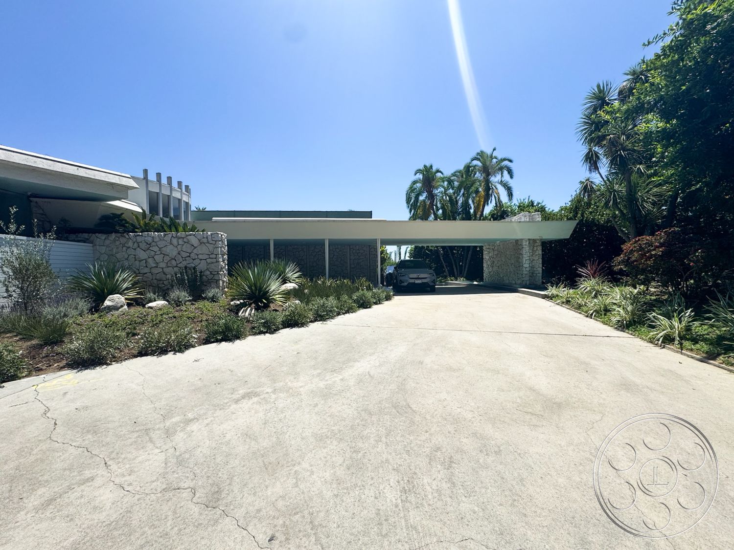 MCM 28 - exterior, palm trees, modern architectural style, concrete driveway, horizontal wood slats, flat roof structure, clear blue sky background, landscaped garden area with succulents, covered carport, stone wall with natural finish