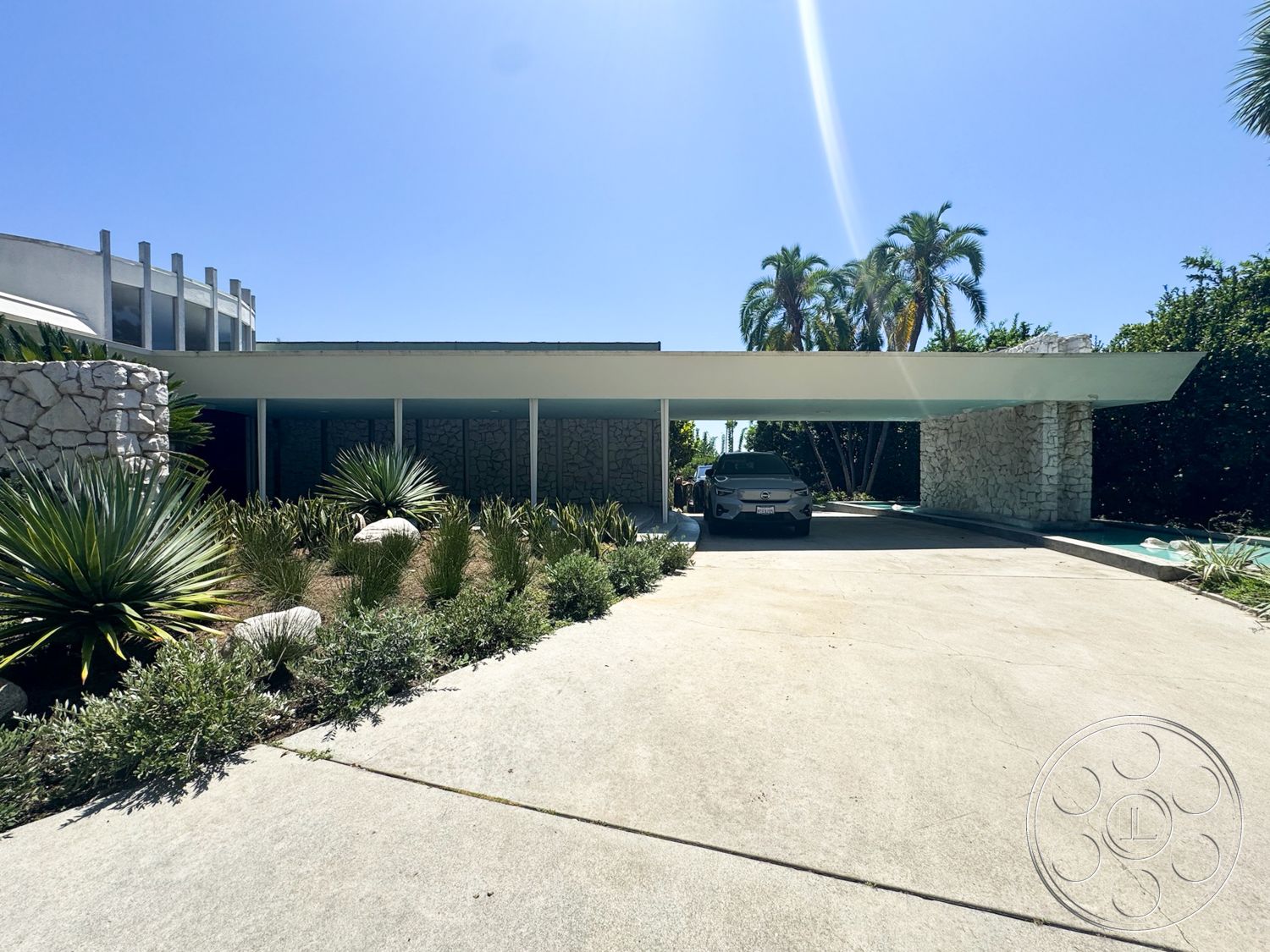 MCM 28 - exterior, concrete driveway, landscaped garden beds, minimalist architectural style, tropical plant landscaping, natural stone feature wall, exposed aggregate concrete surface, palm tree accents, flat roof carport, concrete garden path