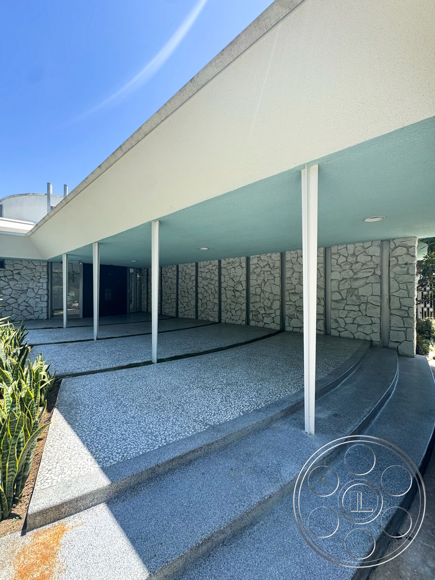 MCM 28 - exterior, flat roof, modern architectural style, stone feature wall, horizontal layout, exposed aggregate concrete driveway, curved concrete steps, white painted soffit, light blue ceiling, landscaped planters with greenery