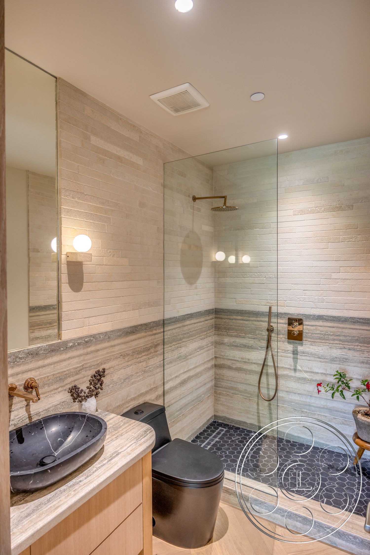 Modern 526 - neutral color palette, wood cabinetry, glass shower enclosure, interior bathroom, textured stone accent wall, hexagonal black tile flooring, pale stone wall treatment, black marble sink, black toilet fixture, brushed gold shower fixture, dimmer recessed lighting