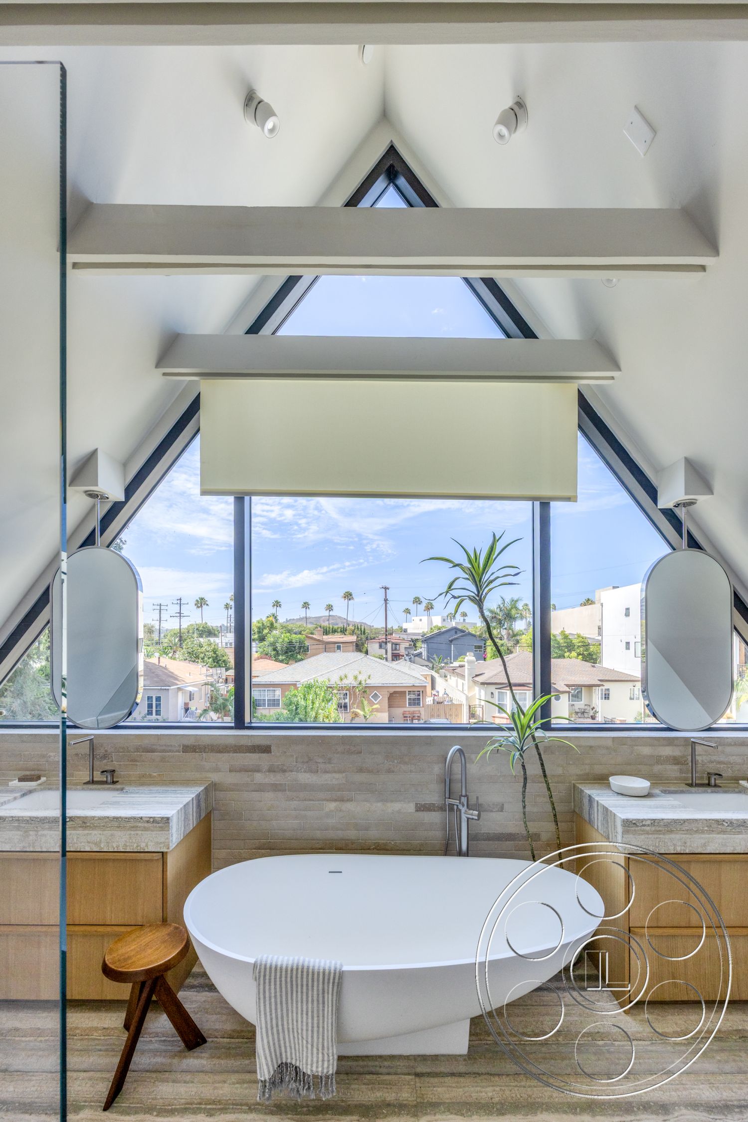 Modern 526 - natural light, textured stone wall, wood cabinetry, freestanding bathtub, glass shower enclosure, vaulted ceiling, wood floor, geometric lighting fixtures, modern bathroom design, quartz bathroom countertops, triangular window, aromatic indoor plant, angled ceiling beams, urban residential view