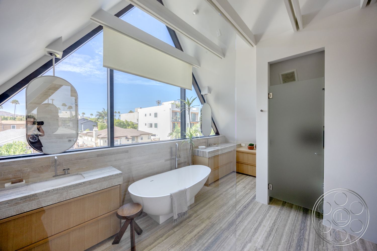 Modern 526 - light hardwood flooring, glass shower enclosure, minimalist design elements, large floor-to-ceiling windows, textured wall treatment, freestanding oval bathtub, sloped ceiling design, wood cabinetry bathroom, double sink vanity with stone countertop, modern mirror with rounded shape, natural light with scenic outdoor view