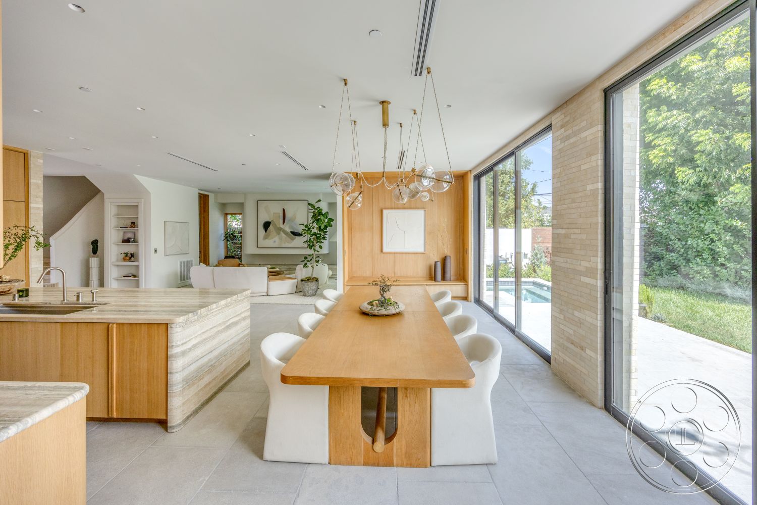 Modern 526 - minimalist decor, upholstered dining chairs, light wood cabinetry, floor-to-ceiling windows, open-concept living space, rectangular dining table, connected indoor-outdoor living, textured stone feature wall, modern chandelier lighting, plant accent decor, natural light-filled dining area, white ceramic tile flooring, granitic kitchen island countertop