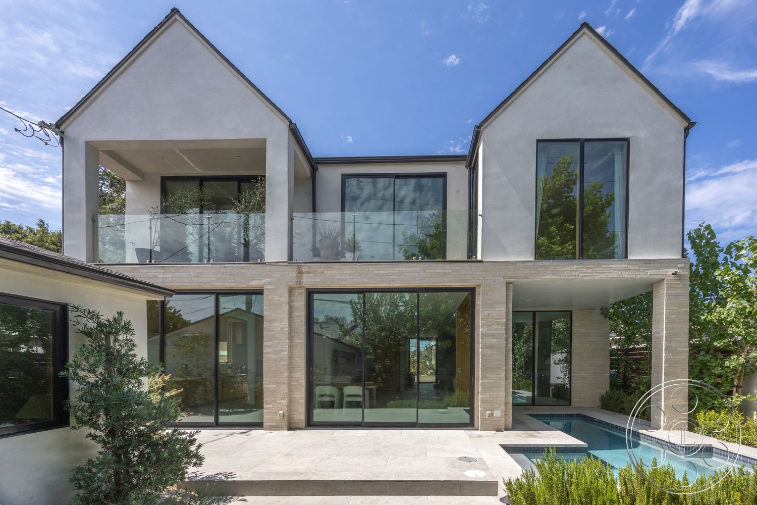 Modern 526 - exterior, flat roof, large glass windows, wooden deck, rectangular swimming pool, floor-to-ceiling windows, geometric shapes, stucco walls, two-story home, minimalist architectural style, brick patio flooring, lush garden landscaping, light-colored exterior finish, modern balcony design, clear glass railings