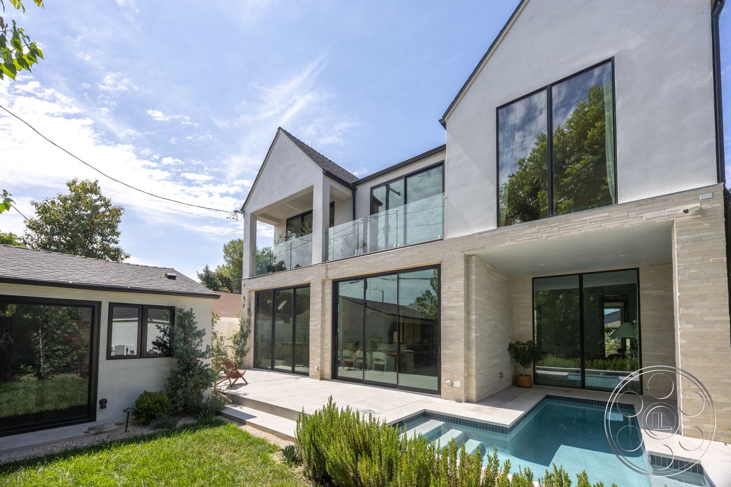 Modern 526 - exterior, landscaped garden, large glass windows, green lawn, outdoor living space, modern home, stone feature wall, concrete patio flooring, stucco exterior walls, rectangle pool, metal balcony railing, pitched roof with gable