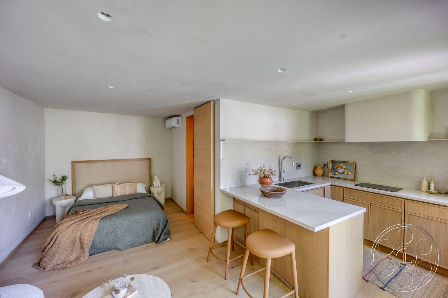 Modern 526 - neutral color palette, minimalist design, open floor plan, light wood cabinetry, natural light from large windows, textured wall treatment, marble kitchen countertops, hardwood bedroom floors, concrete wall finish, wooden breakfast bar, double bed with beige linens, decorative plant on nightstand, sliding wooden door