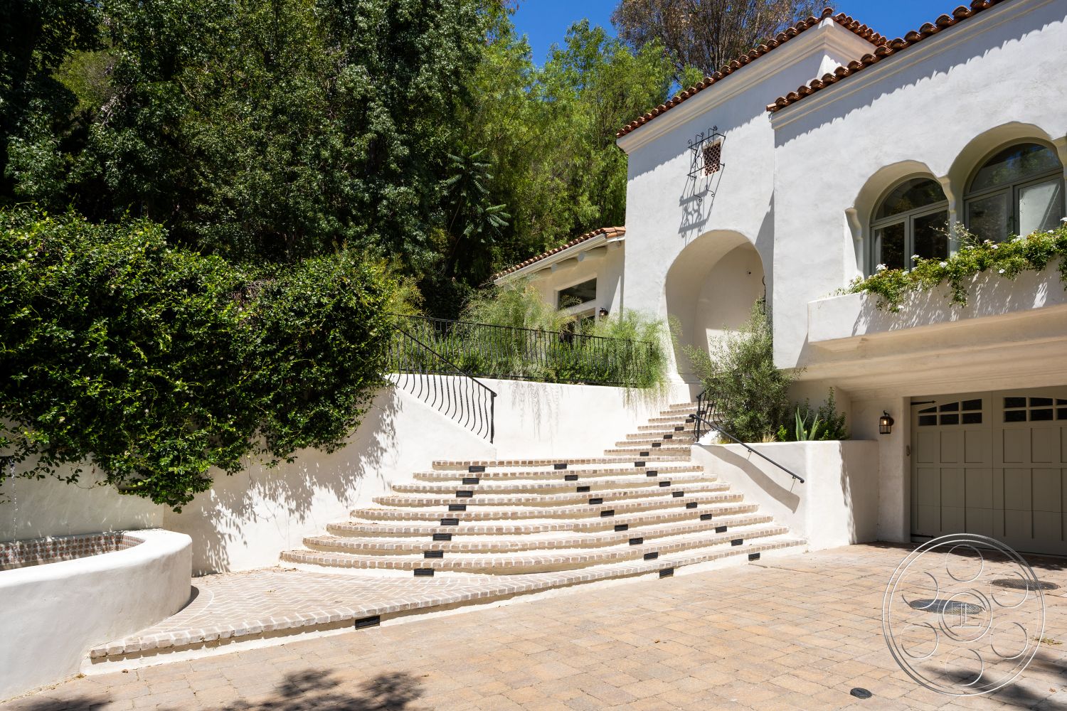 Medit 168 - exterior, lush landscaping, planted greenery, terracotta accents, red tile roof, stucco walls, arched windows, spacious entryway, cobblestone driveway, natural stone retaining wall, outdoor garden space, curved stone steps, black iron railings, visitor parking area, steps with contrasting inlays