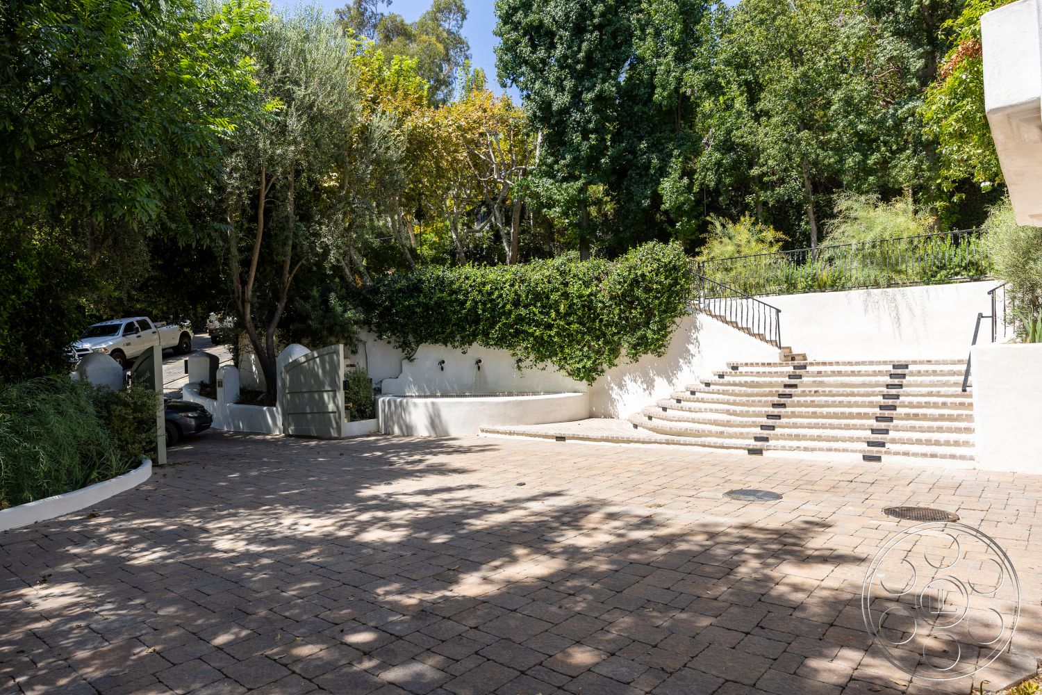 Medit 168 - exterior, white stucco walls, paver driveway, metal railing, surrounding trees, concrete retaining wall, landscaped garden area, rectangular stone steps, property gate, horizontal wooden gate