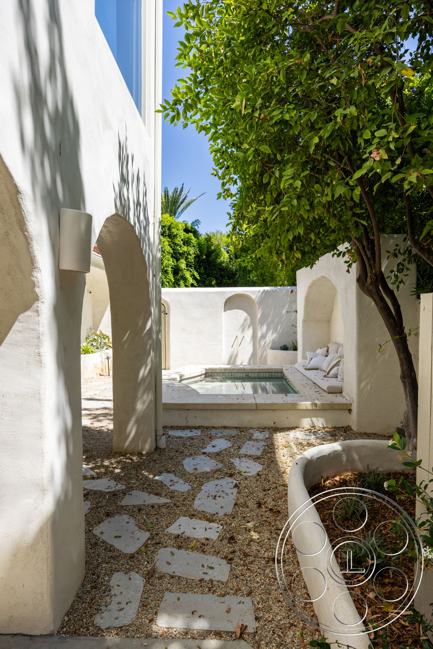 Medit 168 - exterior, stucco walls, arched doorways, integrated seating area, lush greenery landscaping, sunlit courtyard area, rectangular spa, concrete spa border, pebble pathway, whitewashed plaster surfaces, low-profile garden beds, natural stone pathway pavers