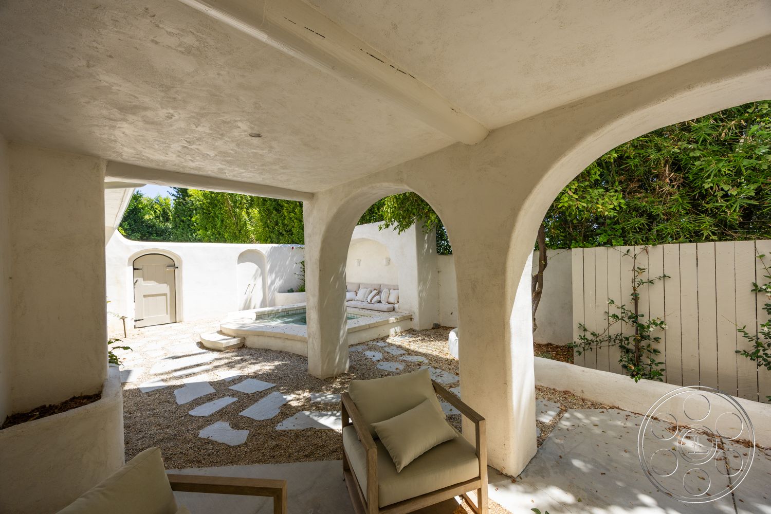 Medit 168 - exterior, wooden door, stone stepping stones, outdoor lounging area, stucco walls, arched doorways, gravel patio flooring, concrete pool edge, constructed seating area, landscaped green setting