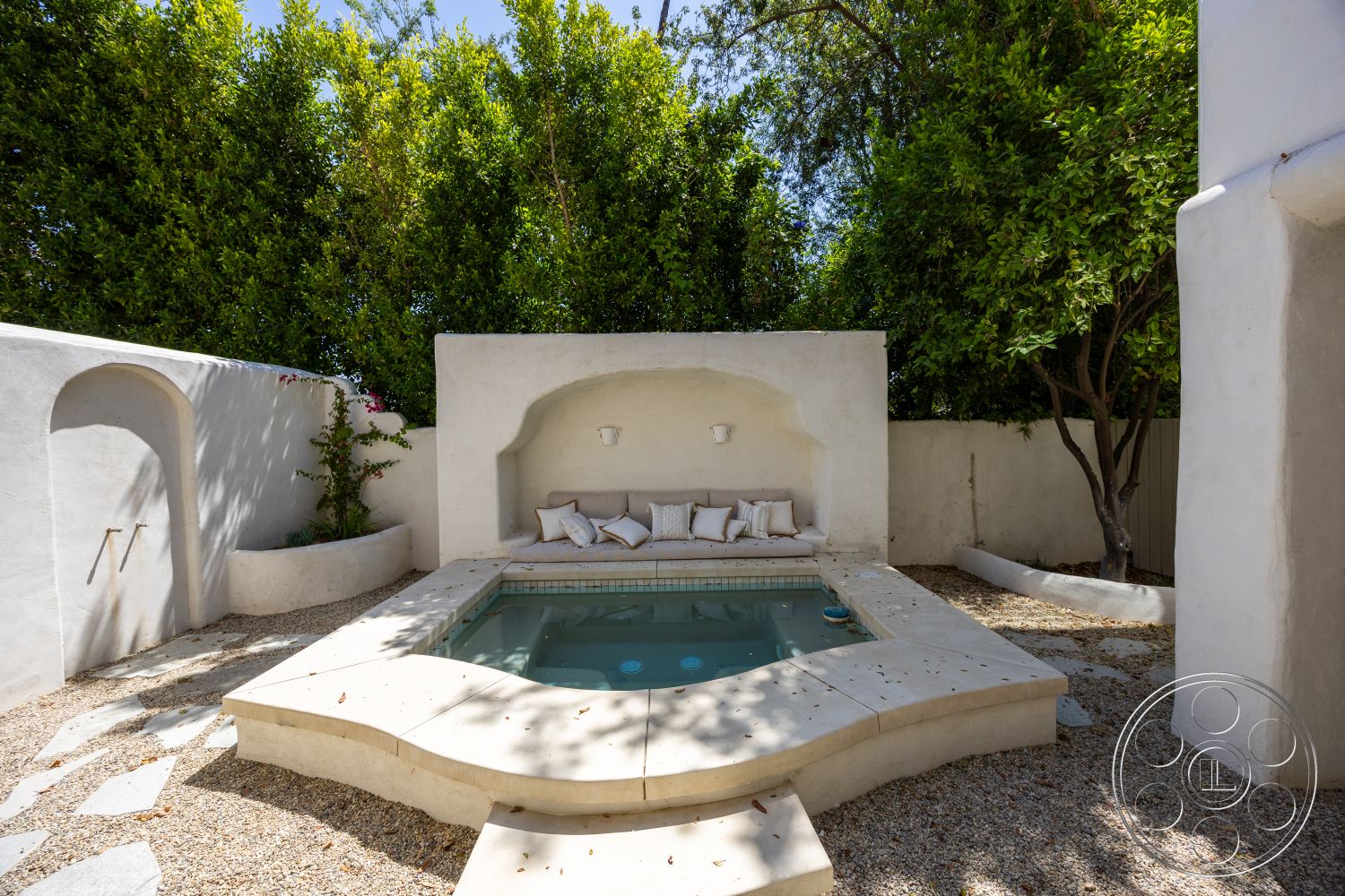 Medit 168 - exterior, curved wall design, minimalist outdoor space, landscaped garden setting, stucco wall finish, gravel patio flooring, sunken hot tub, concrete hot tub surround, rectangular hot tub shape, architectural planter bed, built-in seating with cushions, softscaping with shrubs and trees