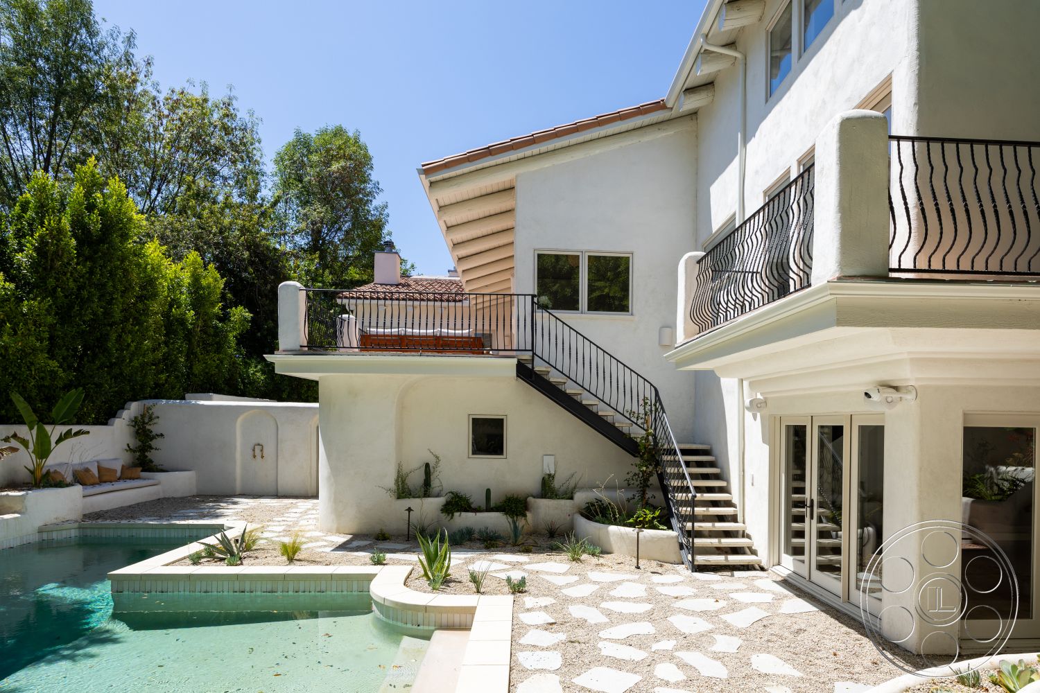 Medit 168 - exterior, exposed wooden beams, rectangular swimming pool, floor-to-ceiling windows, stucco walls, tile roof, sunny outdoor area, landscaped garden beds, curved balcony railing, natural stone patio flooring, staircase with metal railings, desert home setting
