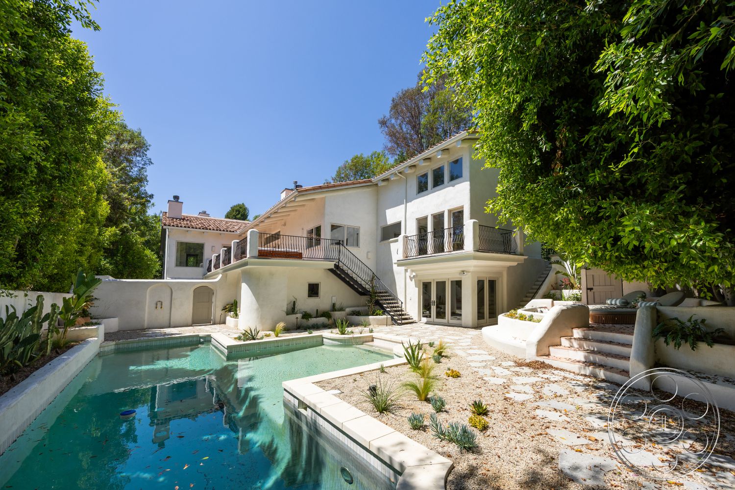 Medit 168 - exterior, landscaped garden, rectangular swimming pool, floor-to-ceiling windows, paved walkway, terracotta roof tiles, two-story house, drought-resistant plants, stone patio flooring, concrete pool border, balcony with metal railing, sunlit outdoor area, stucco house facade, wooden staircase with wrought iron railings, sloping backyard