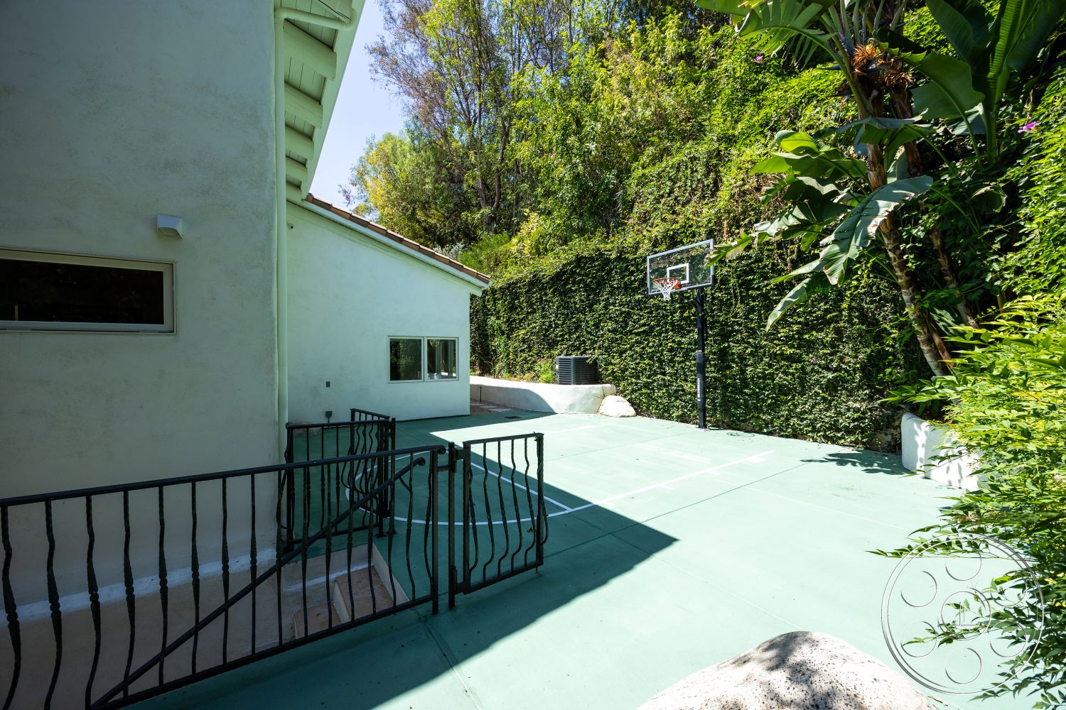 Medit 168 - large windows, exterior, sloped roof, green landscape, tall hedges, wrought iron railing, outdoor sports area, stucco wall finish, decorative stone border, concrete basketball court, metal basketball hoop, integrated air conditioning unit