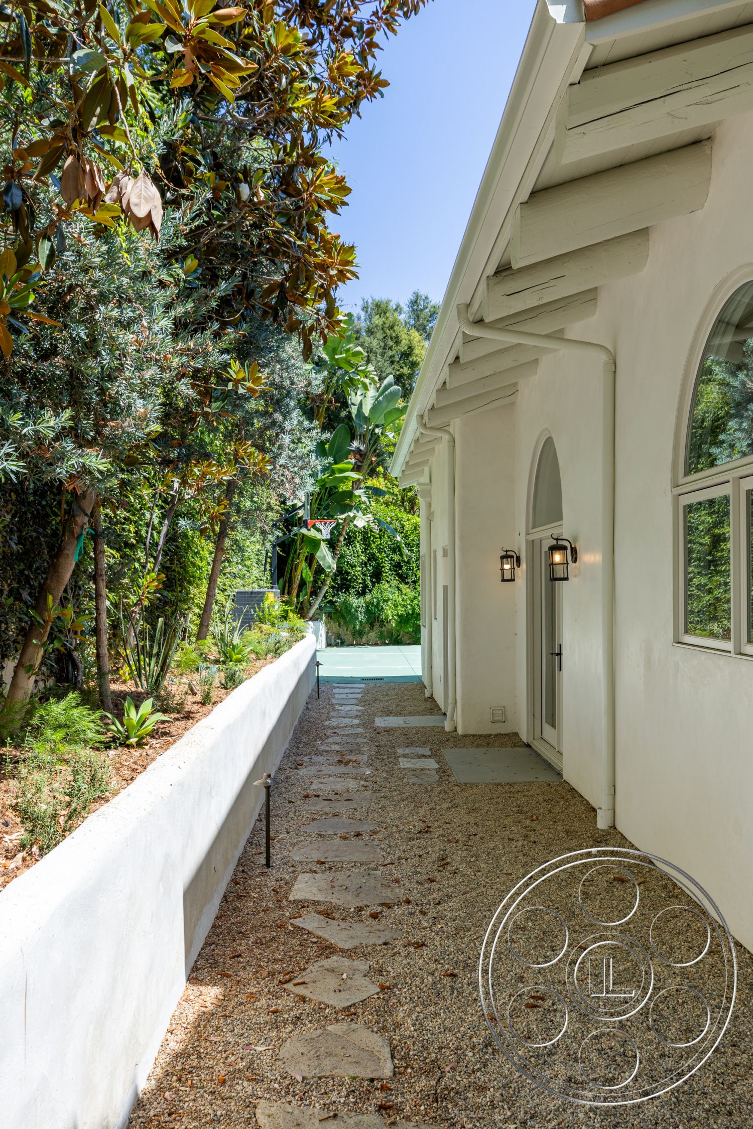 Medit 168 - exterior, concrete wall, gravel pathway, tropical foliage, arched windows, outdoor lighting fixtures, modern residential architecture, landscaped garden setting, stepping stone walkway, wood beam overhang, white stucco finish