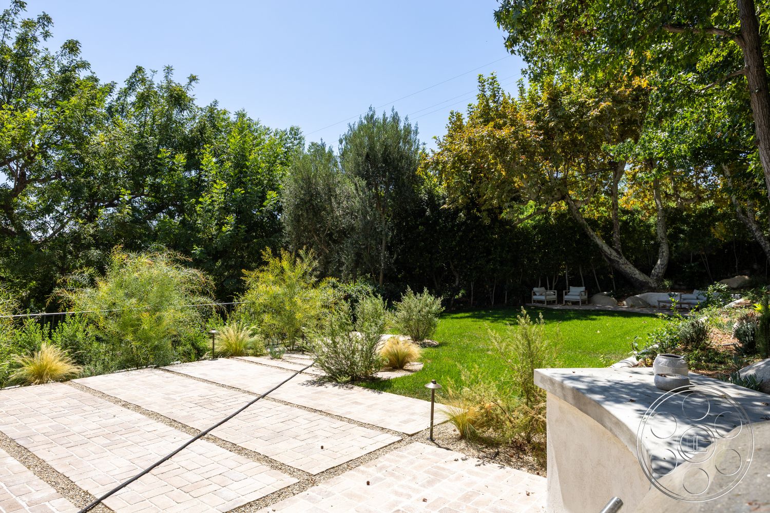 Medit 168 - exterior, mature trees, lush green grass, sunny atmosphere, concrete planter, ornamental shrubs, wooden lounge chairs, landscaped garden area, natural stone boulders, stone patio flooring, rectangular pavers, fenced garden perimeter