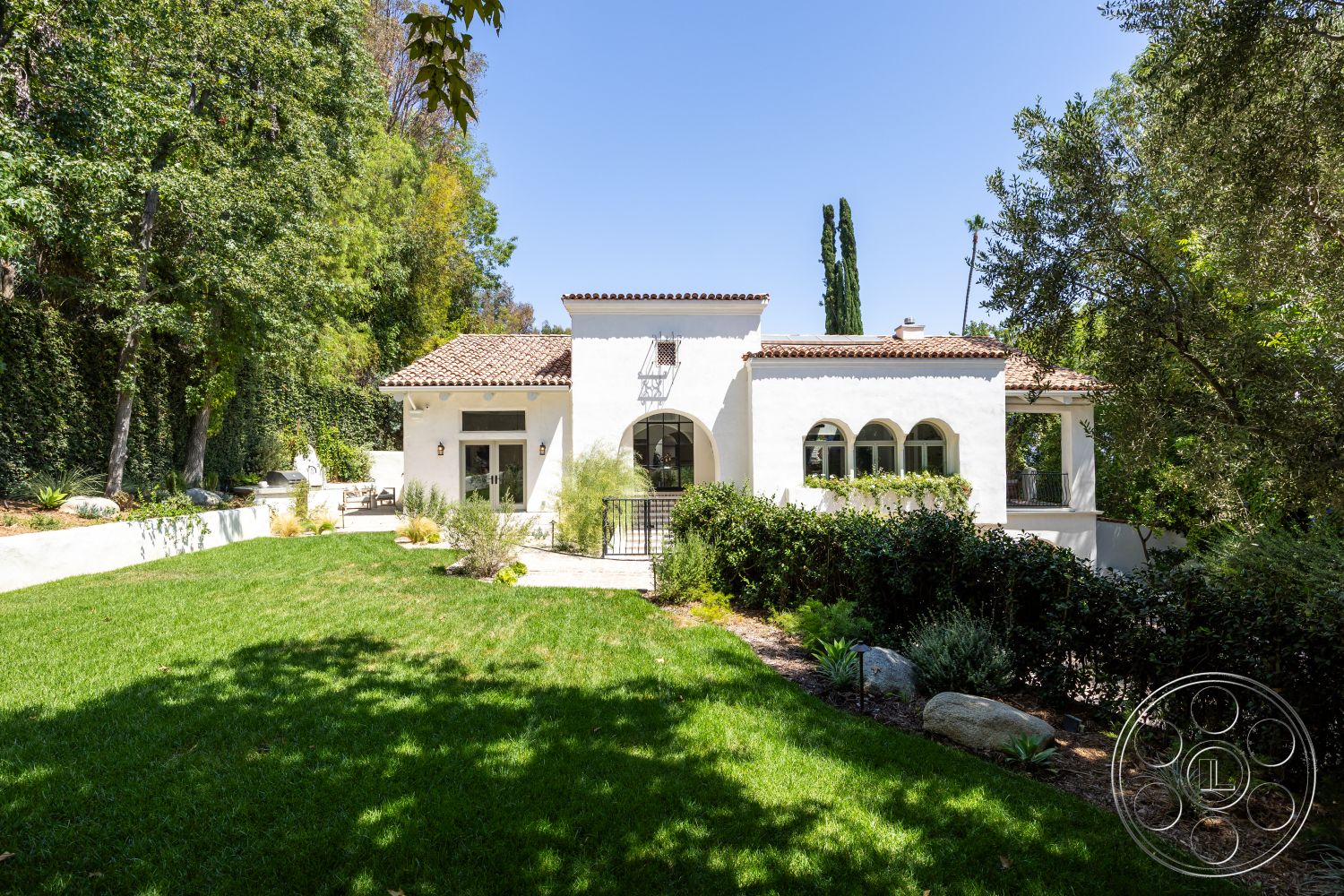 Medit 168 - exterior, landscaped garden, surrounding trees, grassy lawn, mountain backdrop, stucco walls, terra cotta roof tiles, arched windows, wooden front door, Mediterranean architectural style, brick patio flooring, metal outdoor sconces