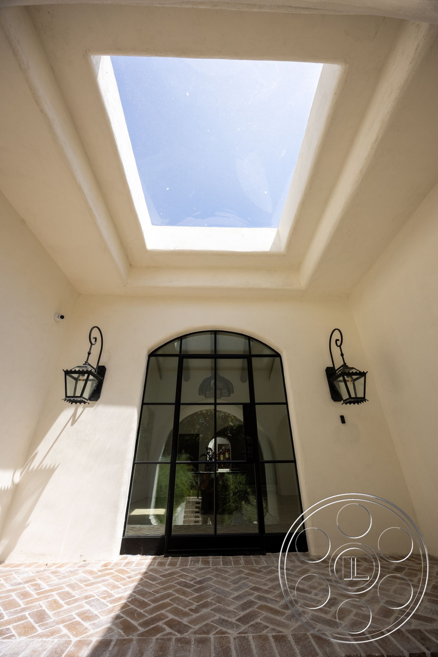 Medit 168 - skylight, arched doorways, exposed concrete ceiling, white plaster walls, glass entry doors, paved entrance, metal lantern light fixtures, herringbone patterned tile flooring, black steel frame