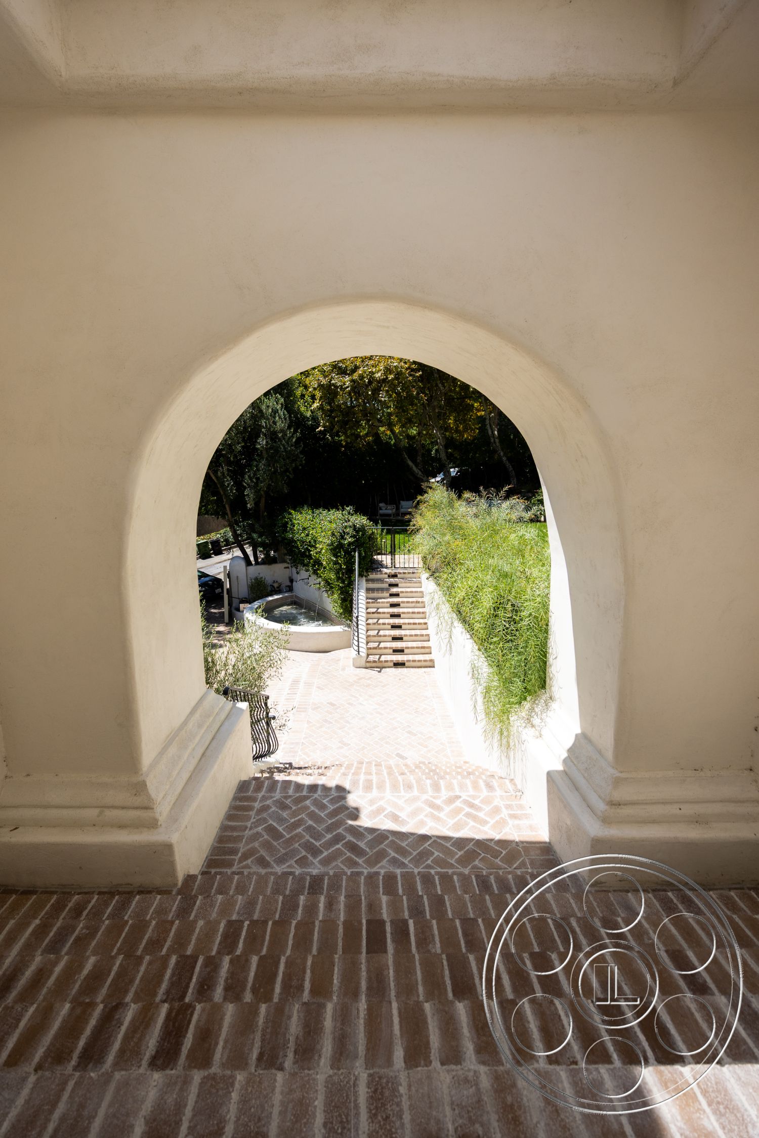 Medit 168 - exterior, landscaped garden, surrounding greenery, arched doorway, stainless steel railing, textured plaster, outdoor stairway, smooth stucco walls, herringbone brick walkway, raised flower beds, nearby water feature