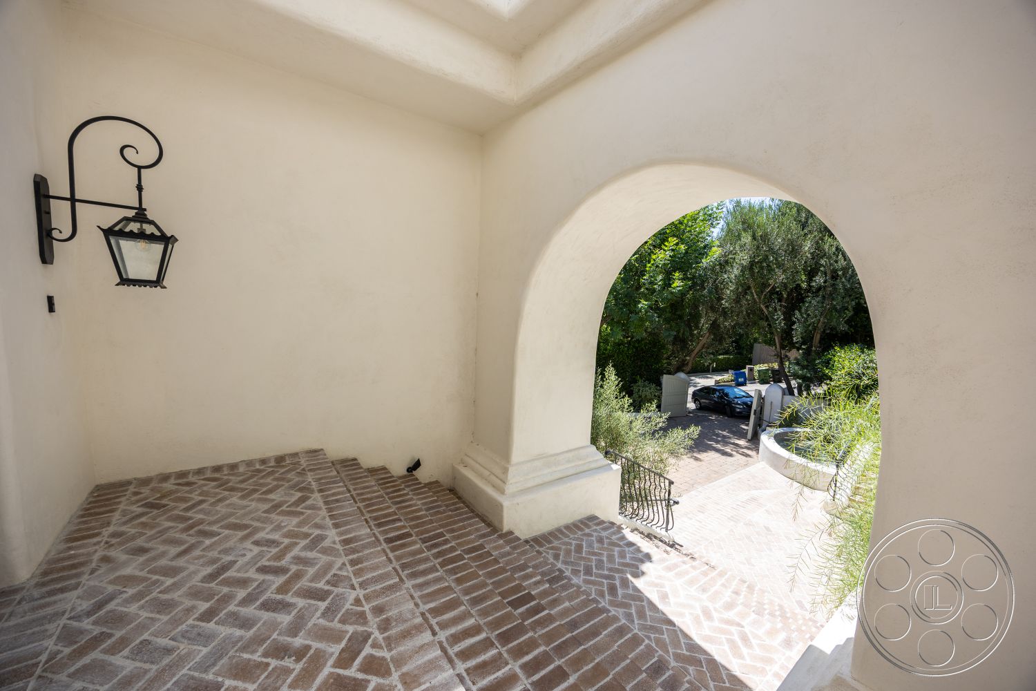 Medit 168 - exterior, paved driveway, surrounding foliage, arched doorway, stucco wall treatment, outdoor lighting fixture, herringbone patterned brick steps, black wrought-iron railing, landscaped green garden, driveway access