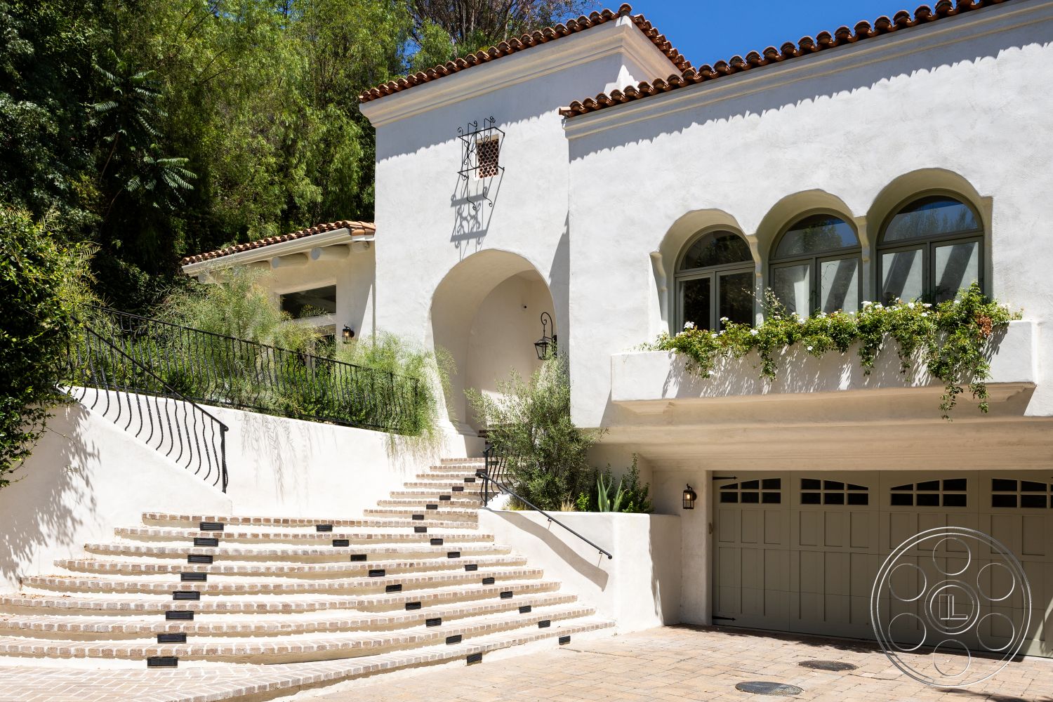 Medit 168 - exterior, landscaped garden, two-car garage, stucco walls, arched entrance, curved staircase, wrought iron railing, decorative window trim, traditional Mediterranean style, tile roof with decorative ridge tiles, stone paver steps, floor-to-ceiling arched windows, plant-filled balcony