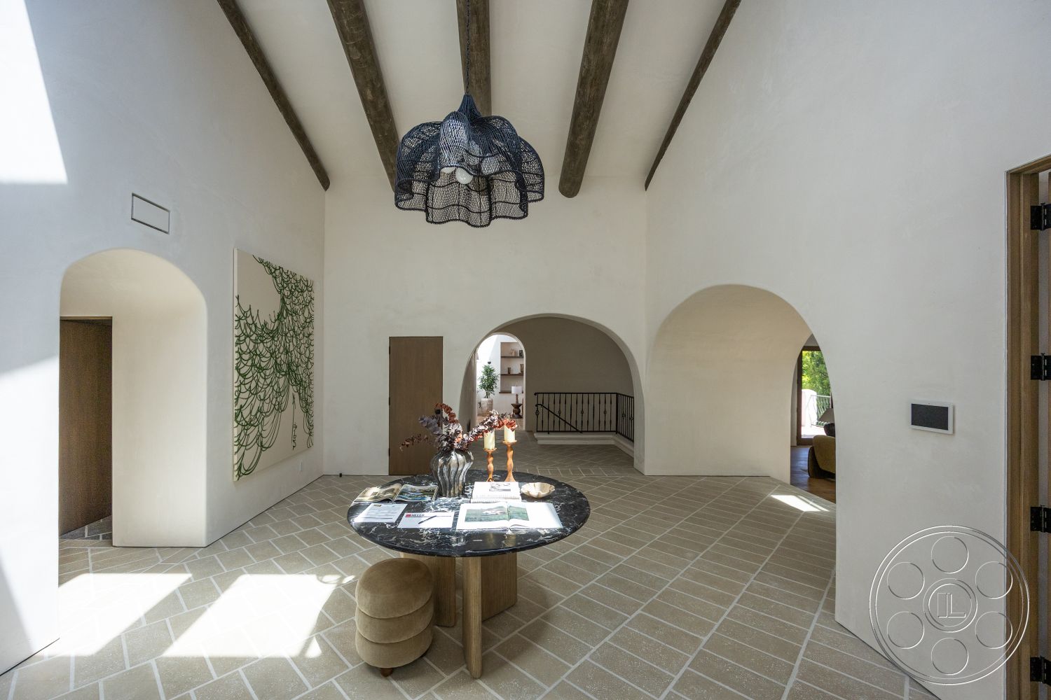 Medit 168 - decorative wall art, arched doorways, round marble dining table, white plaster walls, stone tile flooring, exposed wood ceiling beams, modern pendant light fixture, open floor plan layout, soft upholstered seating, dark wood entrance door