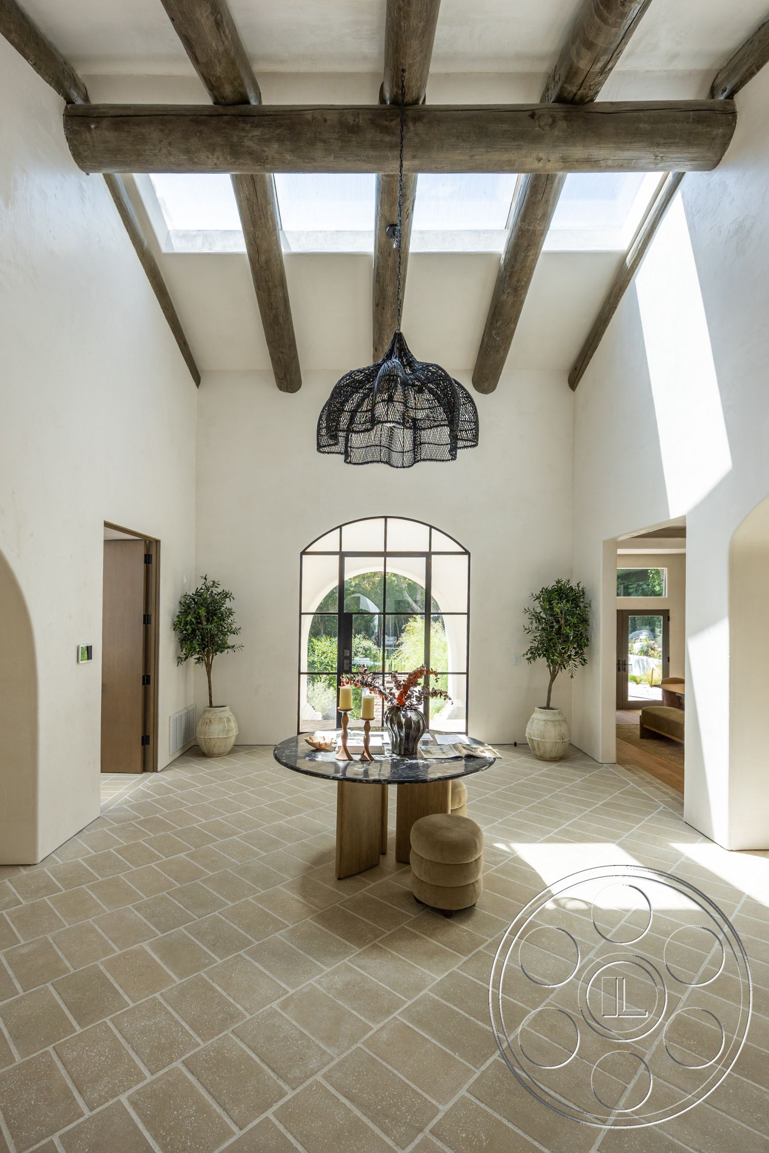 Medit 168 - neutral color palette, open floor plan, modern pendant lighting, wooden side table, textured plaster walls, arched windows, round marble dining table, exposed wood ceiling beams, natural light-filled space, decorative indoor plants, skylight ceiling, stone patterned flooring, black metal window framing