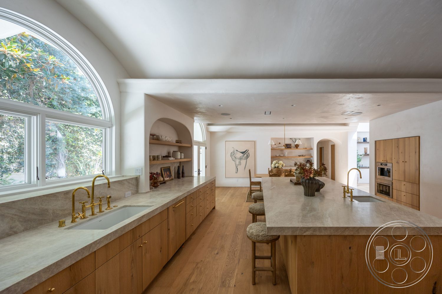 Medit 168 - neutral color palette, natural lighting, light hardwood flooring, light wood cabinetry, arched ceiling, large arched windows, decorative kitchen accessories, open-concept kitchen, minimalist kitchen design, stone kitchen countertops, textured plaster wall finish, floating kitchen shelves, gold-finish faucet fixtures