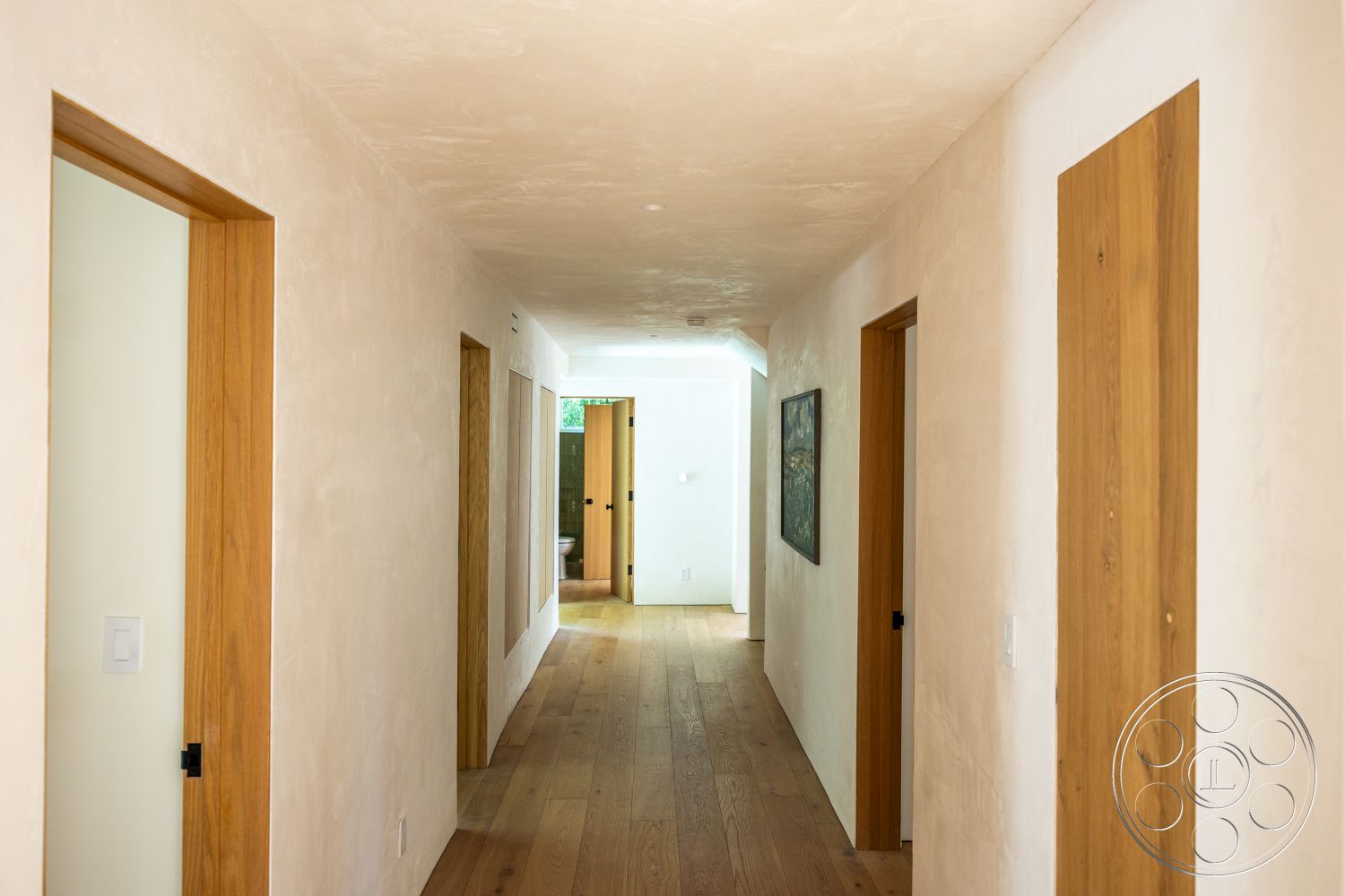 Medit 168 - minimalist design, artwork on wall, light hardwood floor, natural wood trim, smooth plaster wall finish, wooden hallway doors, illuminated hallway, flush-mounted ceiling lighting