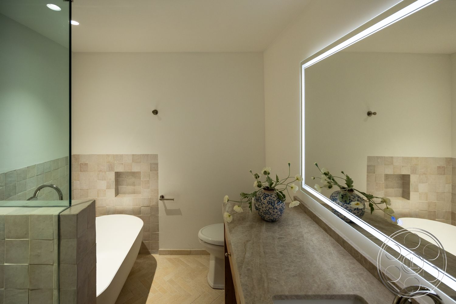 Medit 168 - freestanding bathtub, glass shower enclosure, textured plaster walls, wood vanity, natural stone tile bathroom walls, honed marble countertop, rectangular mirror with LED lighting, chevron patterned tile flooring