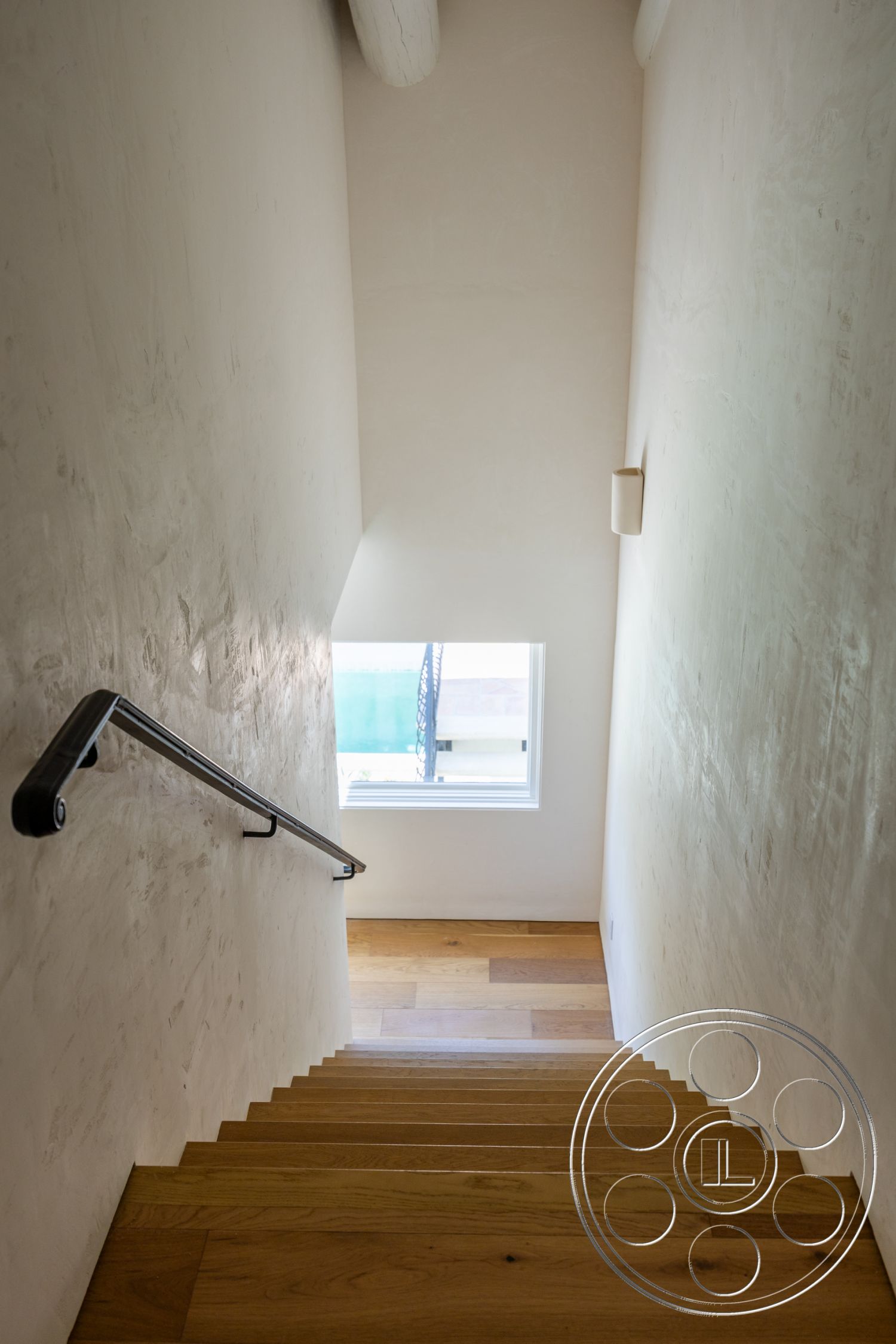 Medit 168 - minimalist design, light hardwood flooring, natural light from window, exposed wood ceiling beams, smooth plaster walls, black metal stair railings, wood stair treads