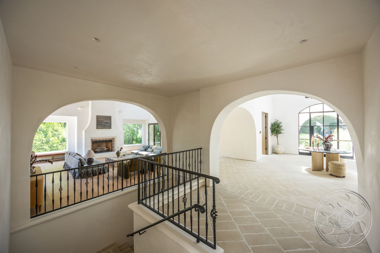 Medit 168 - neutral color palette, open floor plan, floor-to-ceiling windows, vaulted ceiling, arched doorways, natural light-filled space, hardwood floor living room, decorative indoor plants, stone fireplace surround, metal stair railings, exposed plaster walls