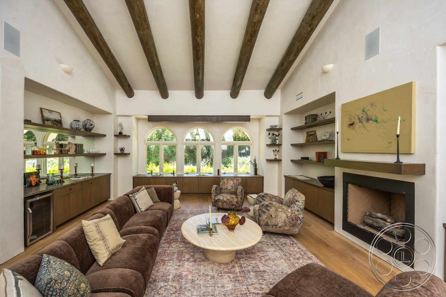 Medit 168 - neutral color palette, round coffee table, decorative wall art, textured plaster walls, natural light from windows, arched windows, exposed wood ceiling beams, hardwood living room floors, cozy living room setting, stone fireplace surround, built-in wooden shelves, plush upholstered sofa, earthy tones and textiles