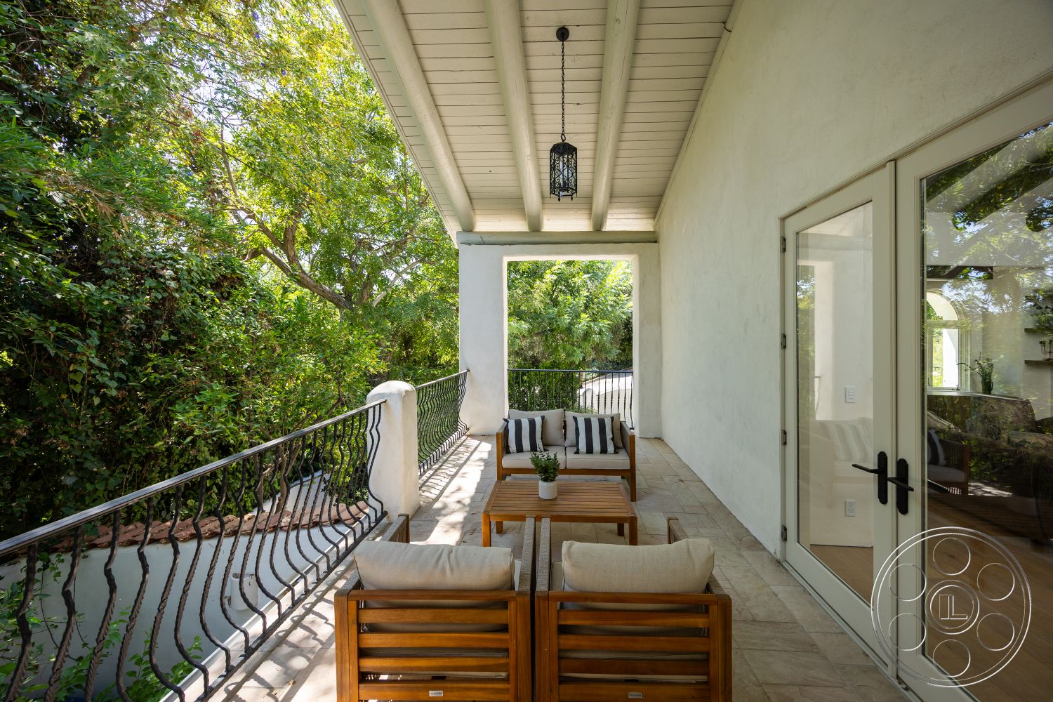 Medit 168 - exterior, textured plaster walls, glass patio doors, wooden outdoor furniture, open-air seating area, wood beam ceiling, natural light exposure, stone patio flooring, arched balcony railing, landscaped greenery surrounding, modern outdoor lighting fixture