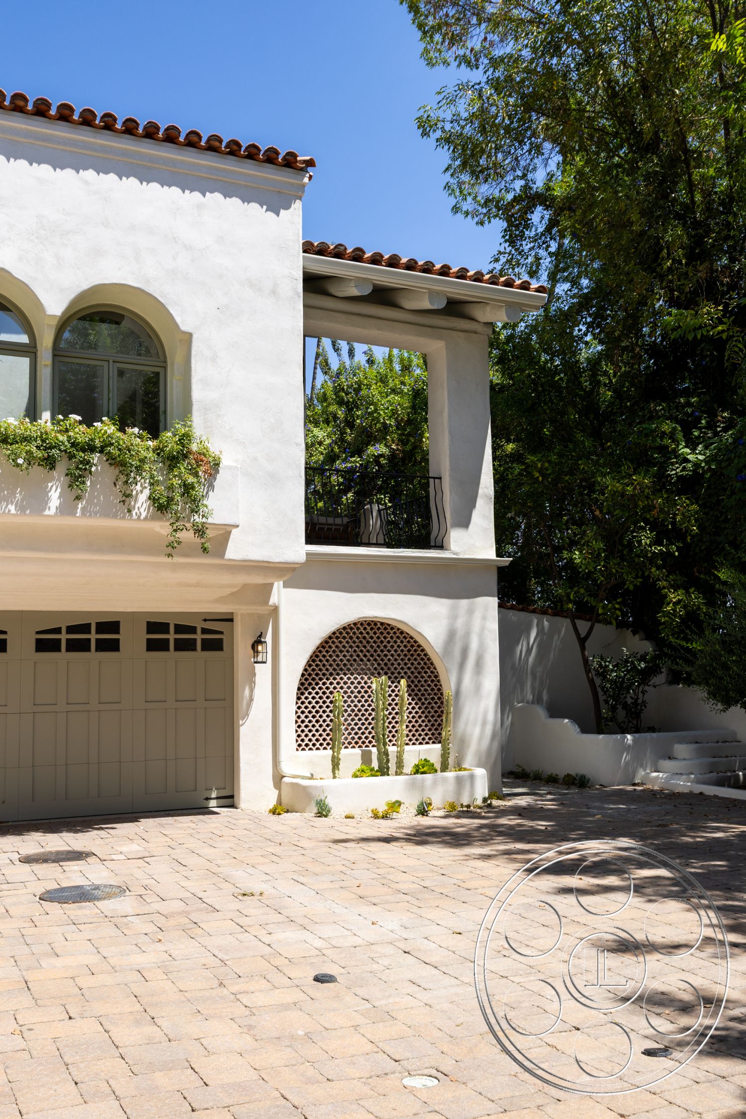Medit 168 - exterior, paver driveway, red tile roof, green foliage backdrop, landscaped garden area, arched window shapes, cacti garden feature, decorative lattice wall, stucco house façade, horizontal beam supports, wall-mounted exterior lighting