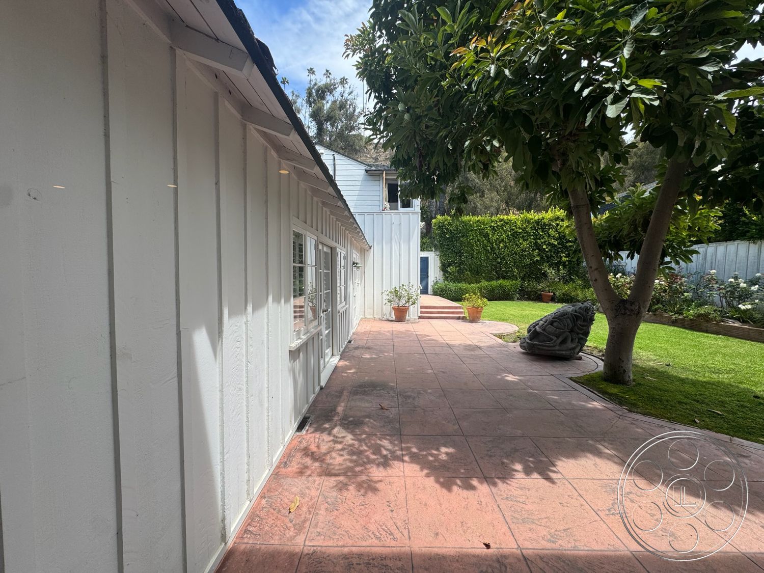 Lloyd Beach House - exterior, mature trees, landscaped hedges, windowed wall, stamped concrete patio, concrete patio flooring, white wood panel siding, lush green garden setting, ornamental planter pots