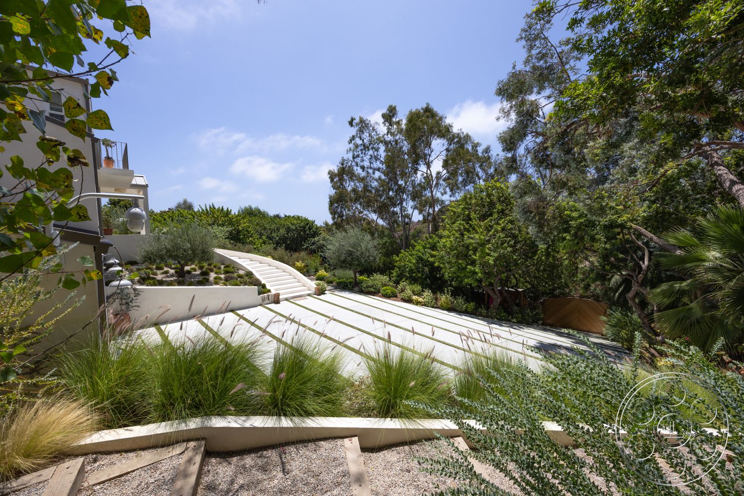 Americana 434 - exterior, smooth concrete surface, concrete pathway, sunny outdoor setting, landscaped garden area, modern home architecture, decorative stone border, curved concrete steps, native plant landscaping, textured gravel ground cover, multi-level outdoor living space, greenery surrounding pathway, softscape garden features