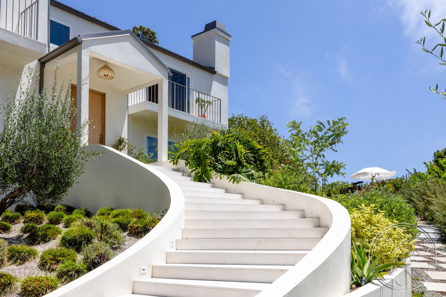 Americana 434 - exterior, white stucco walls, outdoor seating area, stone pathway, single-story home, modern architectural style, wooden front door, gravel ground cover, vaulted roof, landscaped garden area, native plant landscaping, balcony railing, curved concrete staircase