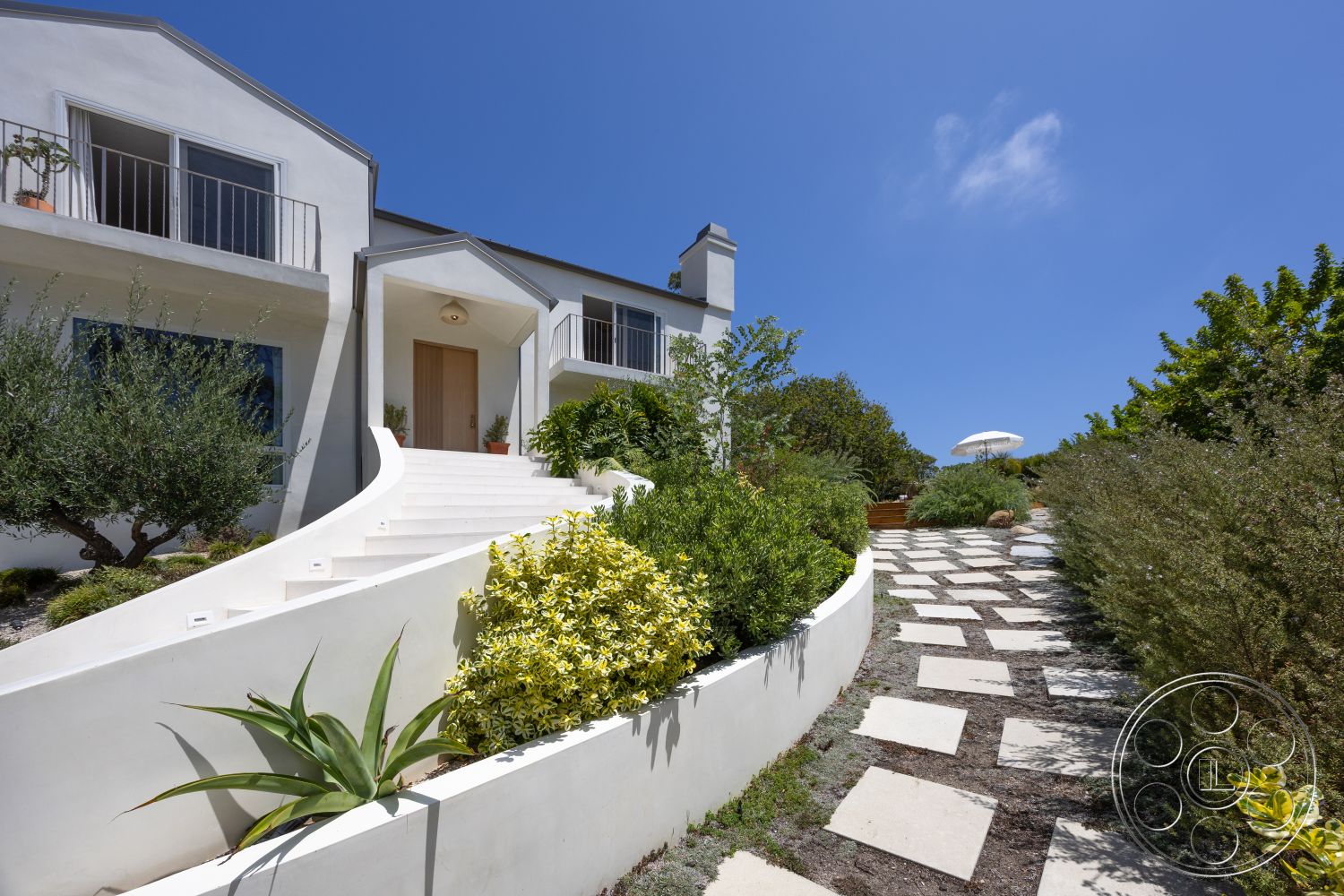 Americana 434 - exterior, white stucco walls, stepping stone walkway, curved concrete steps, green shrubbery accents, landscape garden beds, desert landscape setting, flat roofline, modern balcony railing, view of blue sky, rectangular front porch, recessed door entry